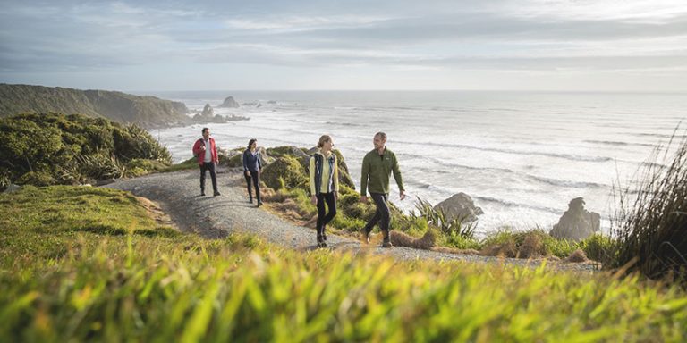 group walking on a track above cliffs overlooking the ocean on a sunny morning