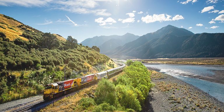 TranzAlpine train on a bend of a rocky river with mountains in the background