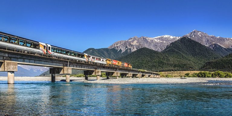 TranzAlpine train crossing a bridge with mountains in the background