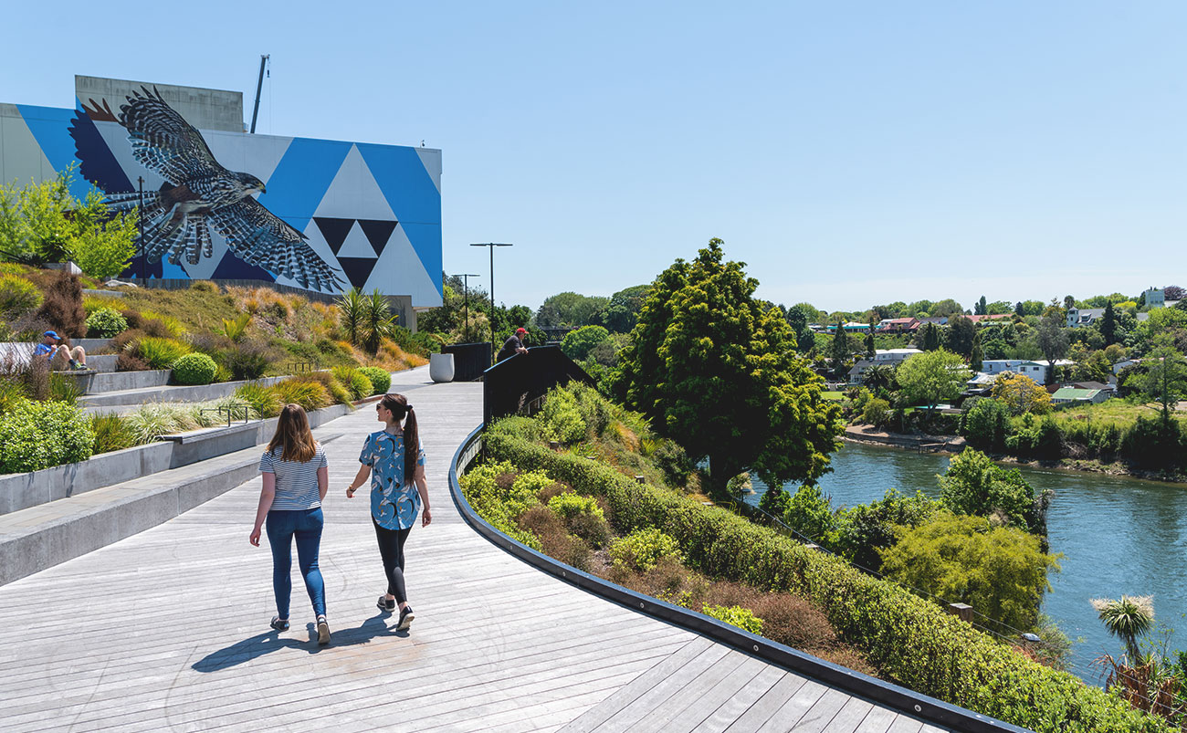 Two women walk along a decked promenade next to the Waikato River in central Hamilton, Waikato, New Zealand